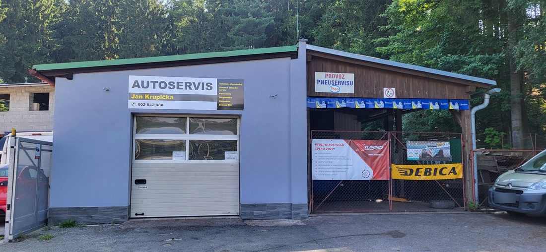 Šedá budova autoservisu s garážovými vraty a vedle krytý pneuservis